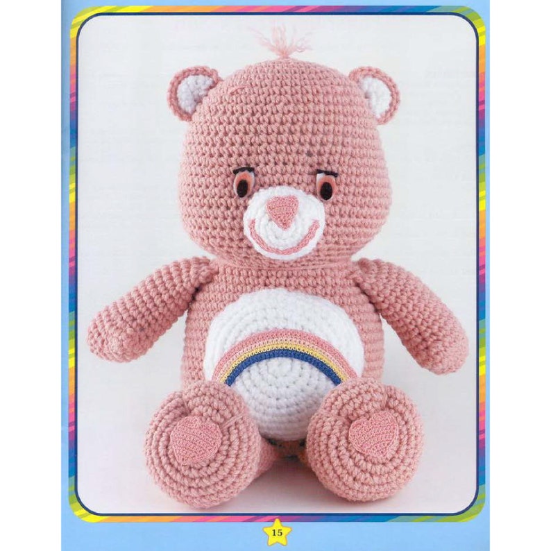 May include: A pink crocheted Care Bear with a rainbow on its belly. The bear has a white face with a pink nose and black eyes.