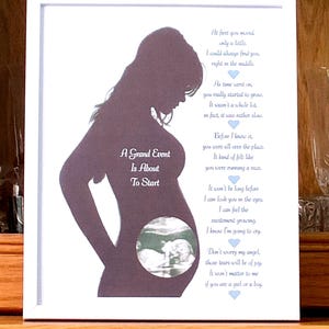 May include: Framed artwork with a dark silhouette of a pregnant person. The artwork includes a sonogram image and a poem about pregnancy. Text on the art reads "A Grand Event Is About To Start".