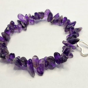 Può includere: Un braccialetto composto da piccole pietre irregolari di ametista in tonalità viola. Il braccialetto ha un ciondolo a forma di cuore color argento. Le pietre sono lunghe circa 1,3 cm.