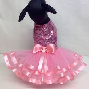 May include: Pink sequined dog dress with a tulle skirt and pink satin ribbon bow.