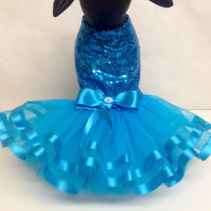 May include: A turquoise blue dog dress with a sequined bodice and a tulle skirt with multiple layers of satin ribbon trim. The dress has a large satin bow at the waist.