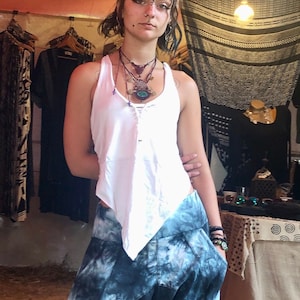Può includere: Una donna indossa una canotta bianca con una gonna a tie-dye blu e bianca. Ha un piercing al naso e diverse collane con ciondoli.
