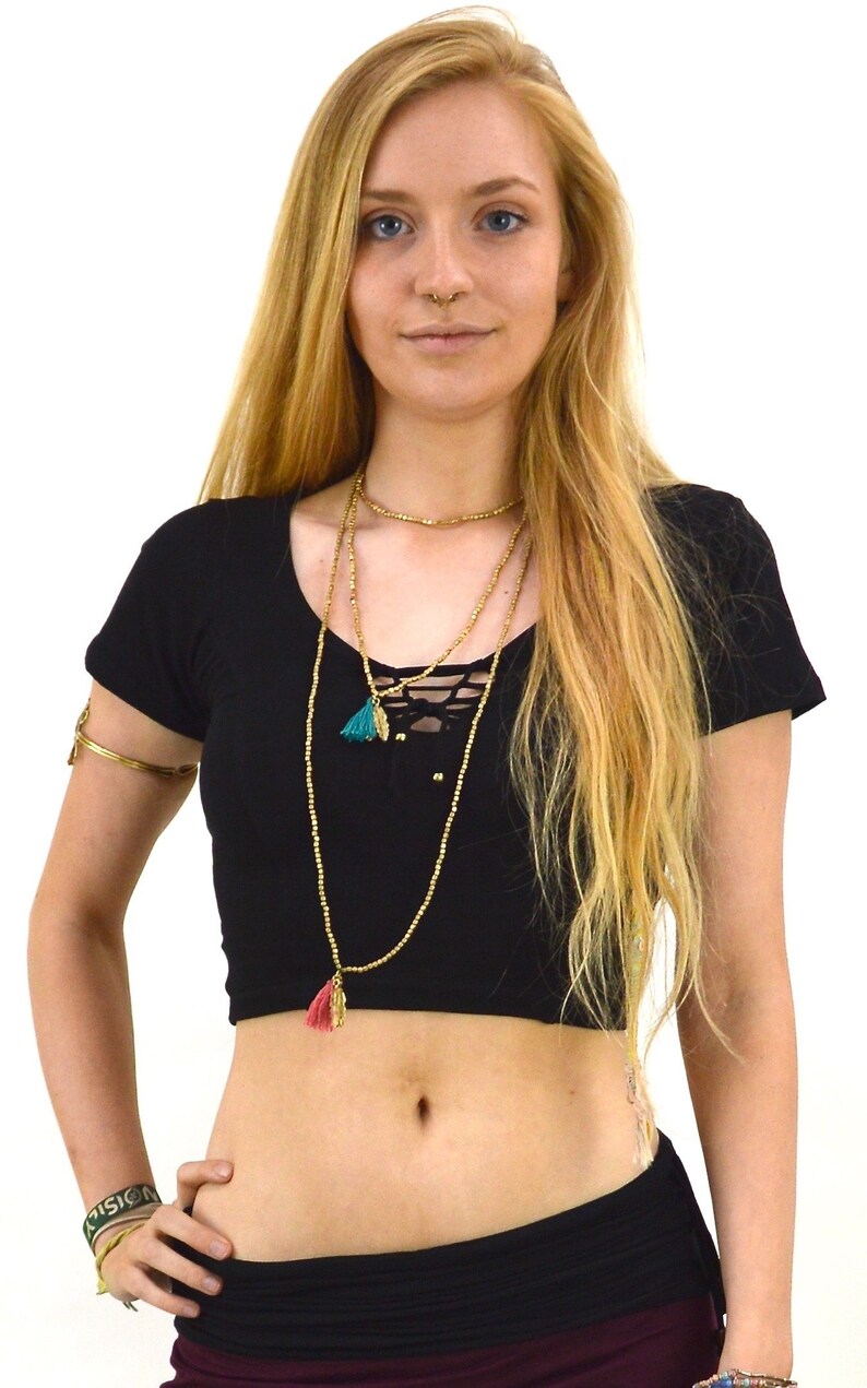 May include: A black crop top with a lace-up detail in the front. The top has short sleeves and a scoop neckline. The model is wearing a gold necklace with multiple strands and a green tassel.