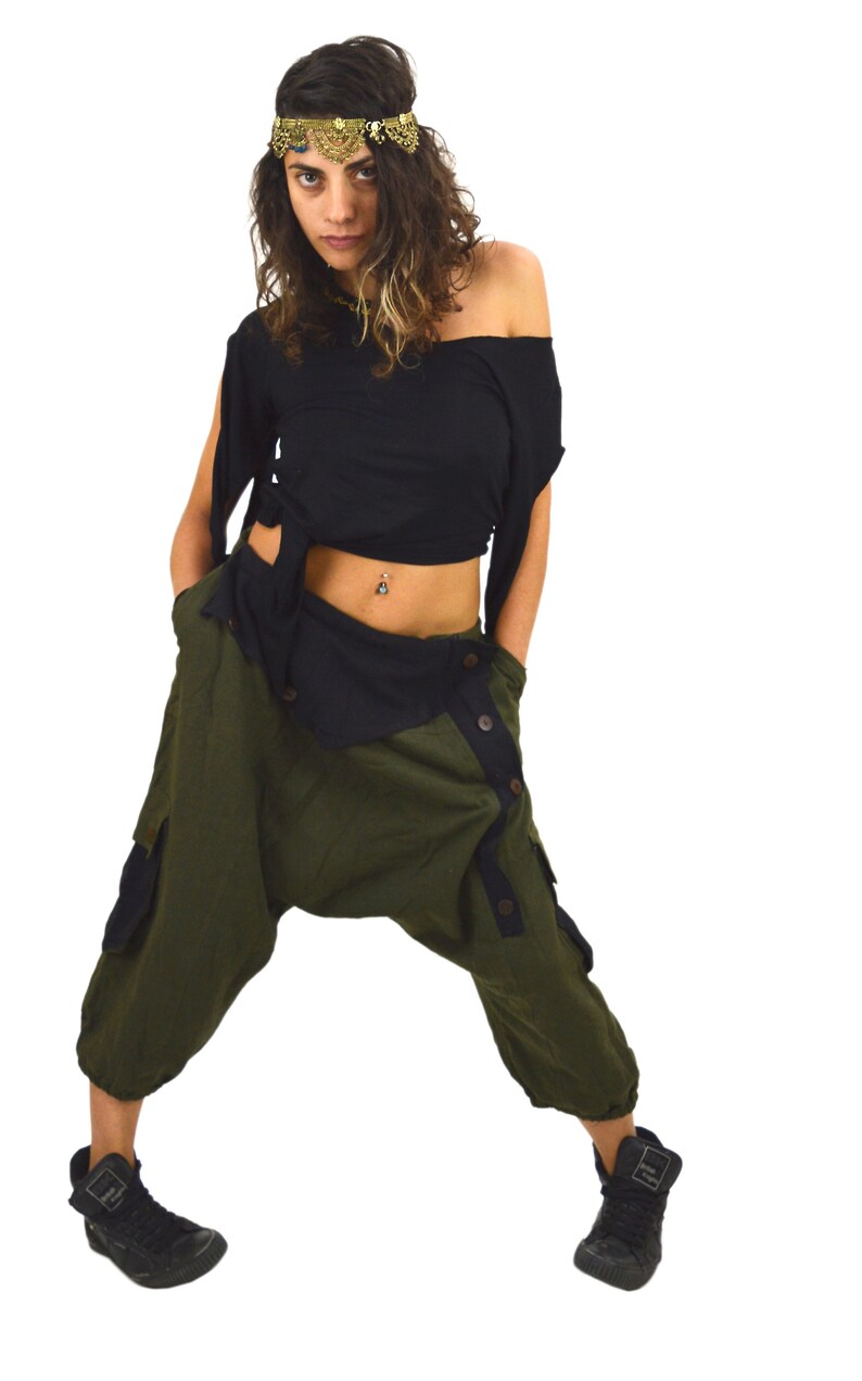 May include: A woman wearing a black crop top with a gold headpiece and olive green trousers with a button closure. The trousers have a black trim and a cargo pocket on the left leg.