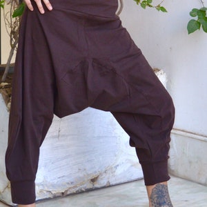 May include: Brown harem pants with a high waist and elastic cuffs. The pants have a relaxed fit with a gathered crotch area. The fabric appears to be a soft, woven material. The pants are worn with a black top.