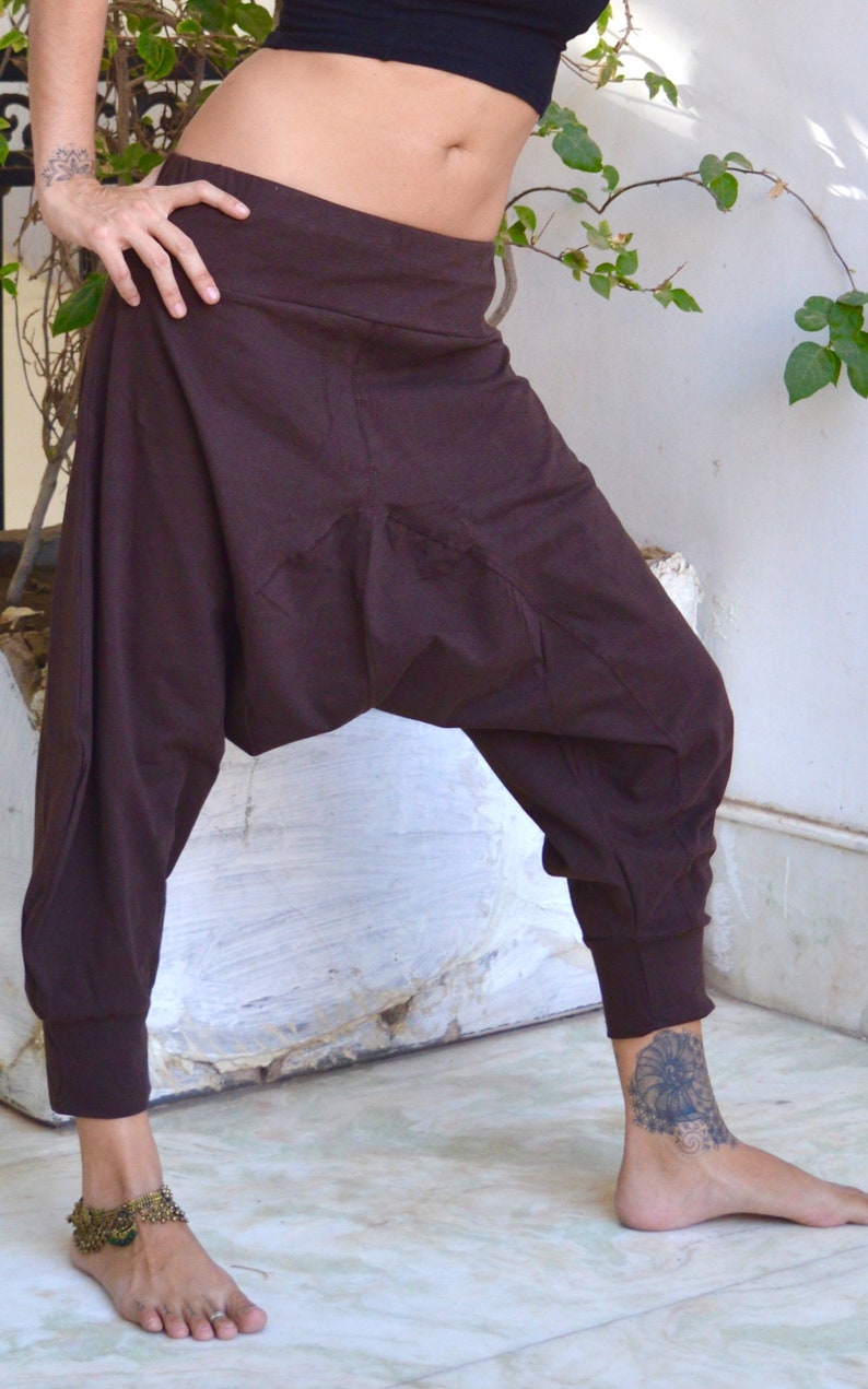 May include: Brown harem pants with a high waist and elastic cuffs. The pants have a relaxed fit with a gathered crotch area. The fabric appears to be a soft, woven material. The pants are worn with a black top.