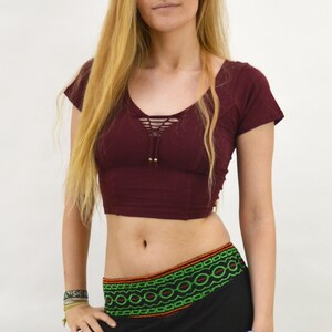 May include: A maroon crop top with a lace-up detail in the front and short sleeves. The top is paired with black pants with a green and orange embroidered waistband.