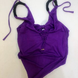 May include: Purple tank top with black straps and gold accents. The straps are tied at the top and the top has a lace-up detail at the front.