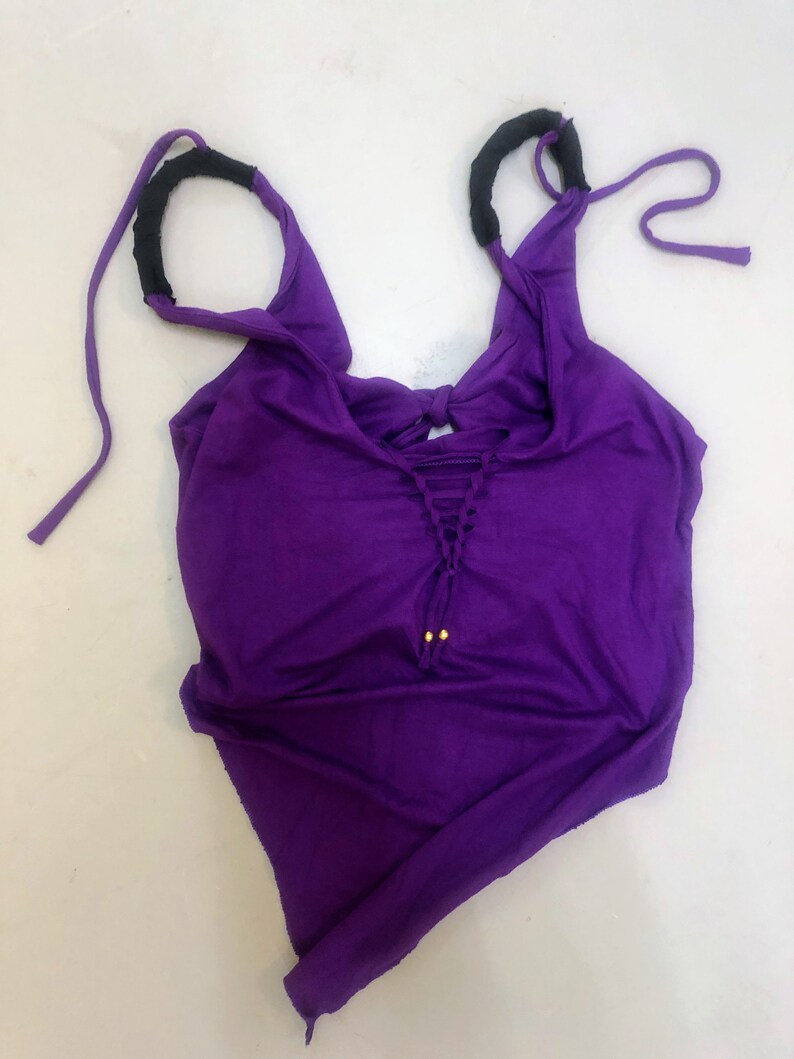 May include: Purple tank top with black straps and gold accents. The straps are tied at the top and the top has a lace-up detail at the front.