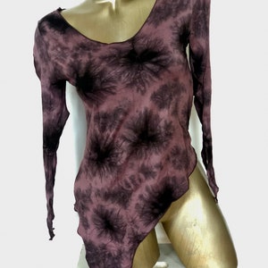 May include: A long-sleeved, tie-dye top in shades of mauve and black. The top features a V-neck and an asymmetrical hemline. The fabric appears lightweight and flowing, with a subtle sheen. The garment is displayed on a mannequin.