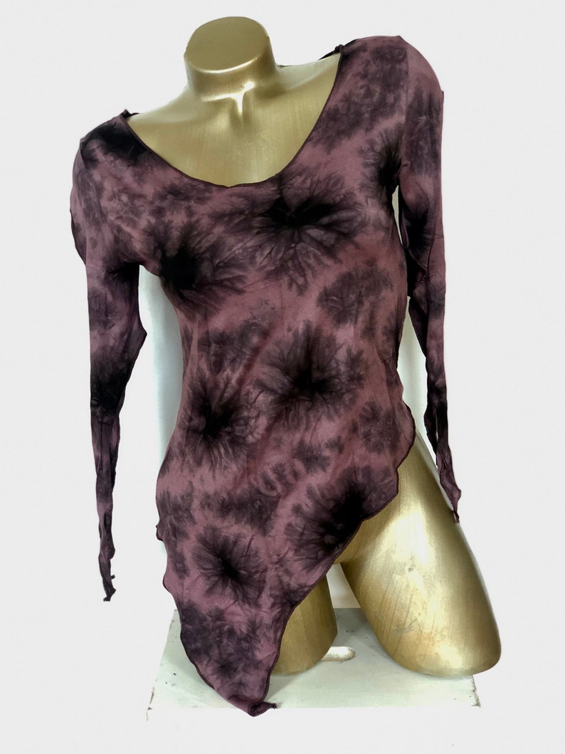 May include: A long-sleeved, tie-dye top in shades of mauve and black. The top features a V-neck and an asymmetrical hemline. The fabric appears lightweight and flowing, with a subtle sheen. The garment is displayed on a mannequin.