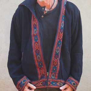 Puede incluir: Una chaqueta negra con capucha, cierre de cremallera y ribetes de colores con patrones geom&eacute;tricos. La chaqueta tiene un corte holgado y est&aacute; hecha de una tela suave y c&oacute;moda.