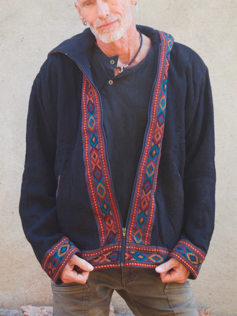 Puede incluir: Una chaqueta negra con capucha, cierre de cremallera y ribetes de colores con patrones geom&eacute;tricos. La chaqueta tiene un corte holgado y est&aacute; hecha de una tela suave y c&oacute;moda.