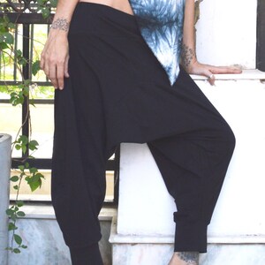 May include: Black harem pants with a cuffed ankle and a loose, comfortable fit. The pants are paired with a tie-dye blue and white top. The outfit is casual and suitable for yoga or everyday wear.