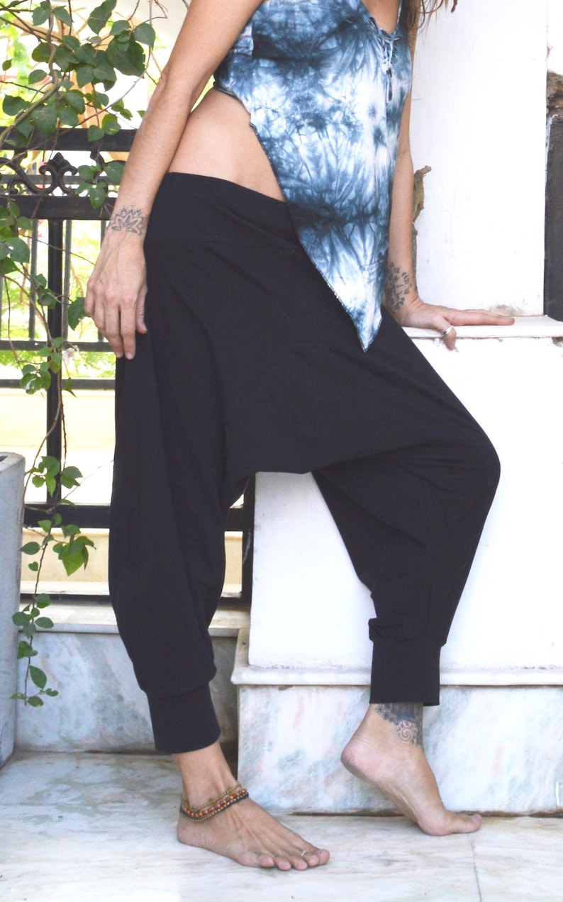 May include: Black harem pants with a cuffed ankle and a loose, comfortable fit. The pants are paired with a tie-dye blue and white top. The outfit is casual and suitable for yoga or everyday wear.