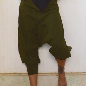 May include: Olive green harem pants with a relaxed fit. The pants have a gathered ankle cuff and a loose, baggy design. The model is wearing a black top. The pants are made of a soft, comfortable material.