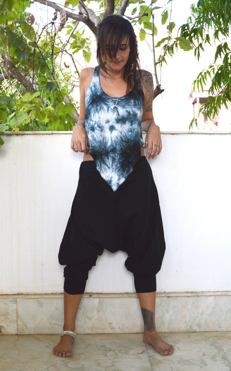 May include: A tie-dye tank top in shades of blue and black paired with black harem pants. The pants have a loose, baggy fit with a gathered ankle. The outfit is casual and comfortable.