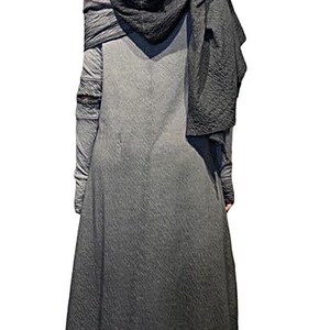 Puede incluir: Un abrigo largo con capucha gris oscuro con una apariencia texturizada. El abrigo presenta mangas largas y un detalle de hombro drapeado. El dobladillo es asim&eacute;trico y la persona lleva zapatos negros.