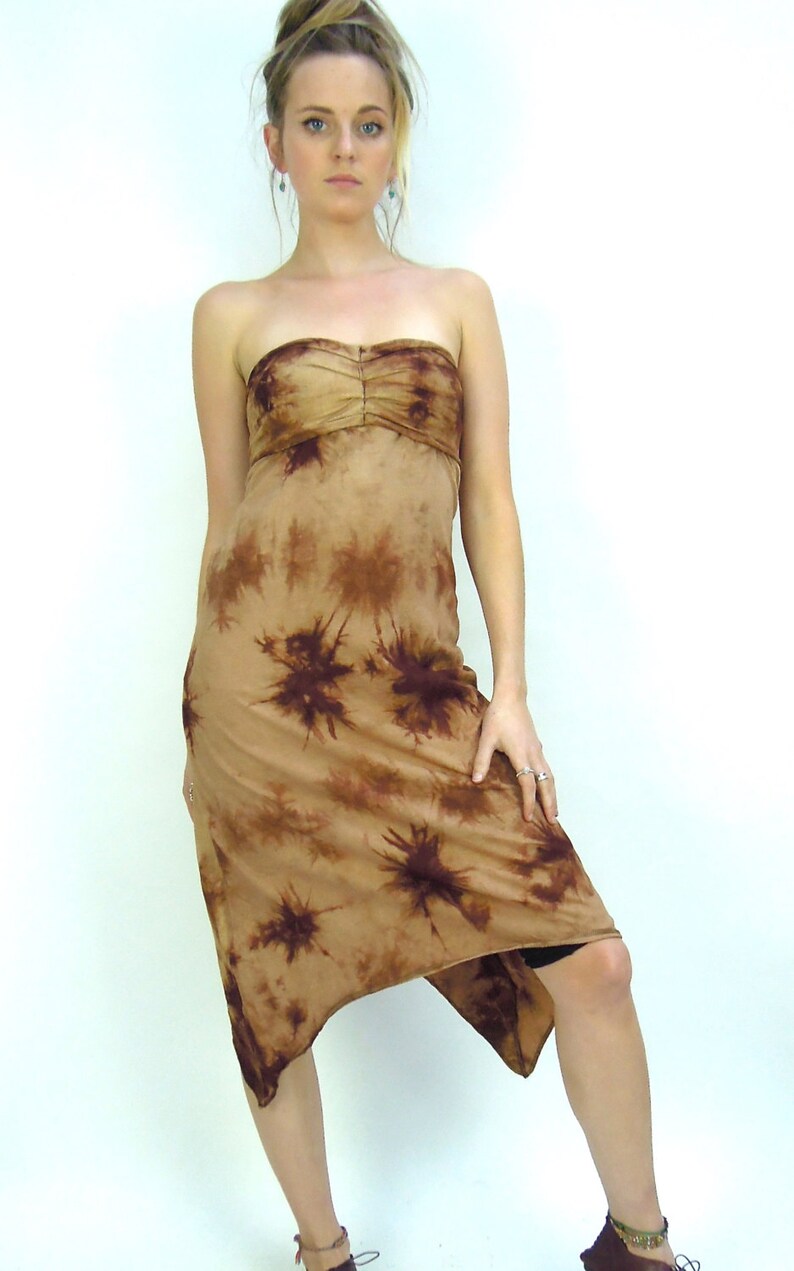 May include: A strapless midi dress with a tie-dye design. The dress has a tan background with dark brown starburst patterns. The bodice is gathered, and the asymmetrical hemline falls to the mid-calf. The dress is made of a soft, flowing fabric.