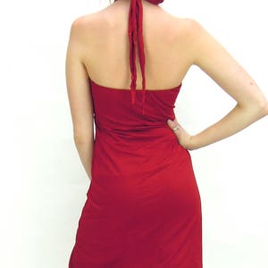 May include: A red halter dress with an asymmetrical hemline. The dress is tied at the neck with matching red fabric. The back of the dress is open, and the fabric flows down the body.
