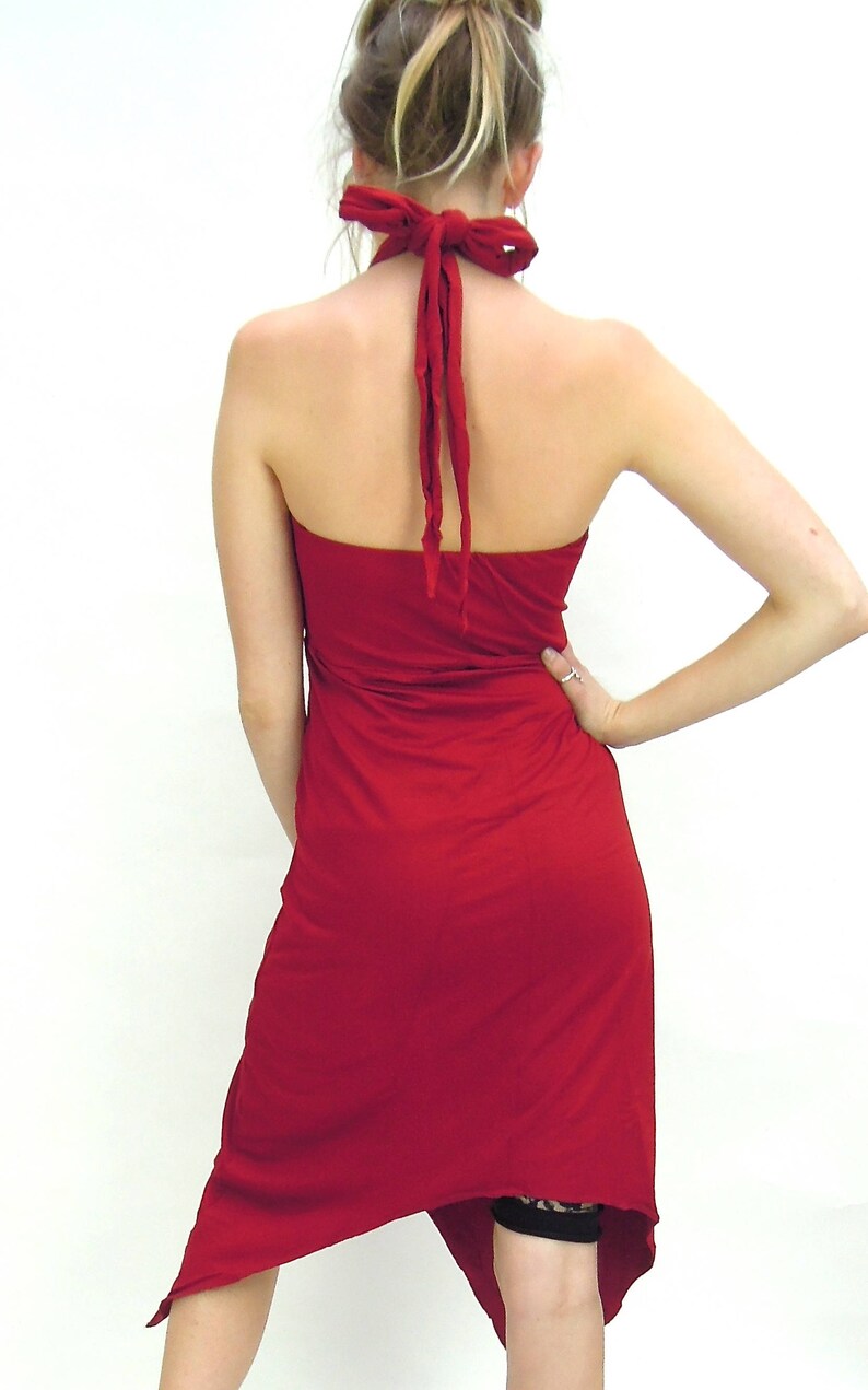 May include: A red halter dress with an asymmetrical hemline. The dress is tied at the neck with matching red fabric. The back of the dress is open, and the fabric flows down the body.