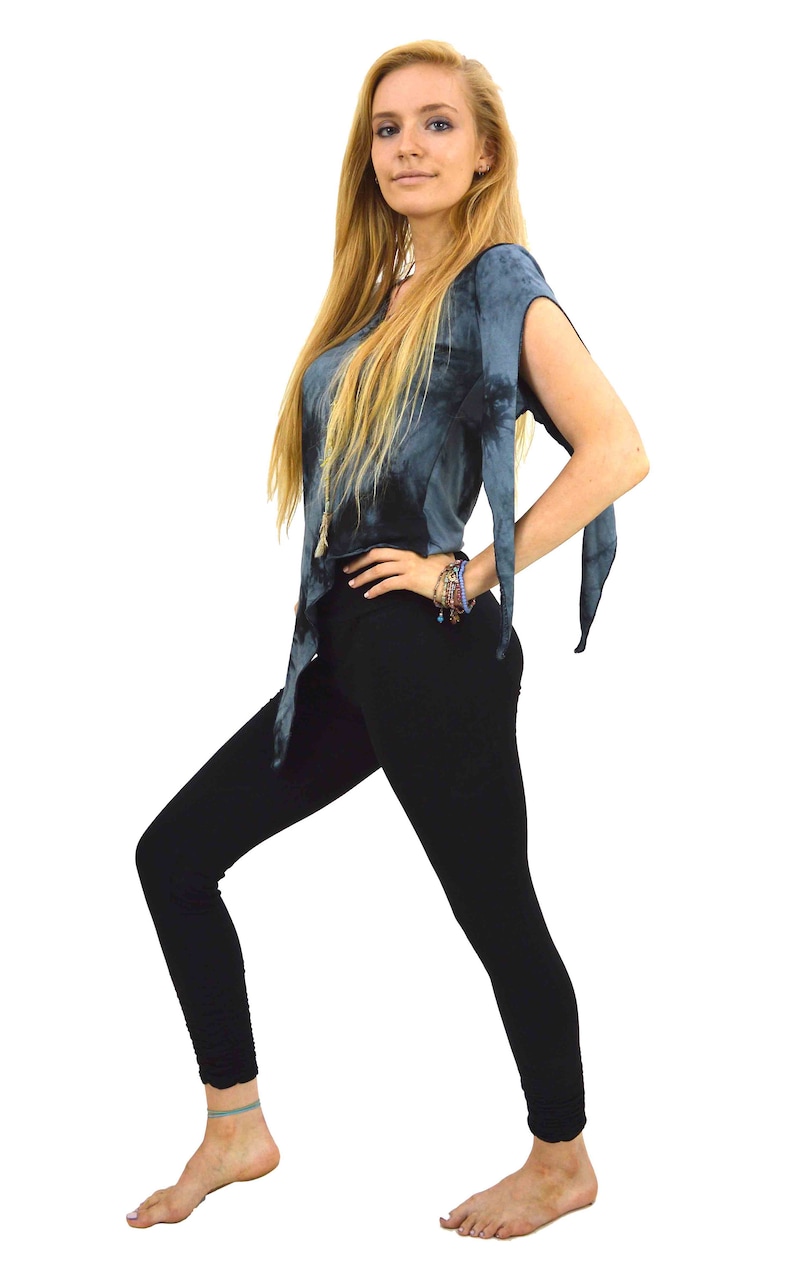 May include: A woman wearing a tie-dye top and black leggings. The top is a dark blue with a flowing design, and the leggings are form-fitting. The woman is barefoot, with a bracelet on her wrist.