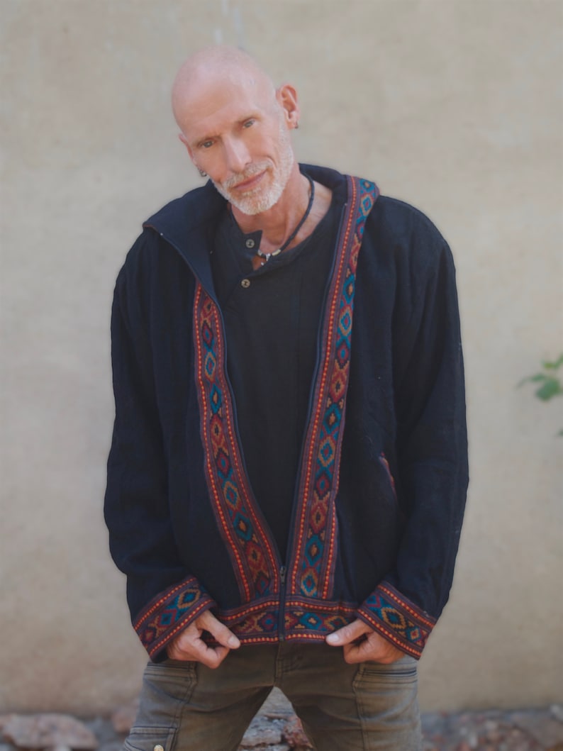 Puede incluir: Una chaqueta negra con capucha, cierre de cremallera y ribetes bordados de colores. La chaqueta tiene un corte holgado y un estilo informal.