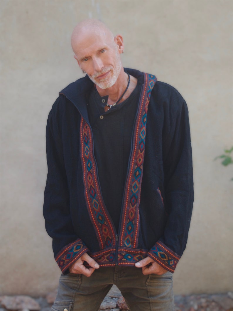 Puede incluir: Una chaqueta negra con capucha, cierre de cremallera y ribetes bordados de colores. La chaqueta tiene un corte holgado y un estilo informal.