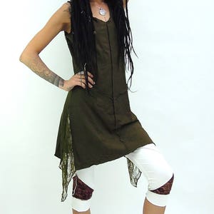 May include: An olive green hooded tunic dress with a sleeveless design. The dress features a lace trim on the sides and is paired with white capri leggings with lace accents. The outfit is completed with black ankle boots.