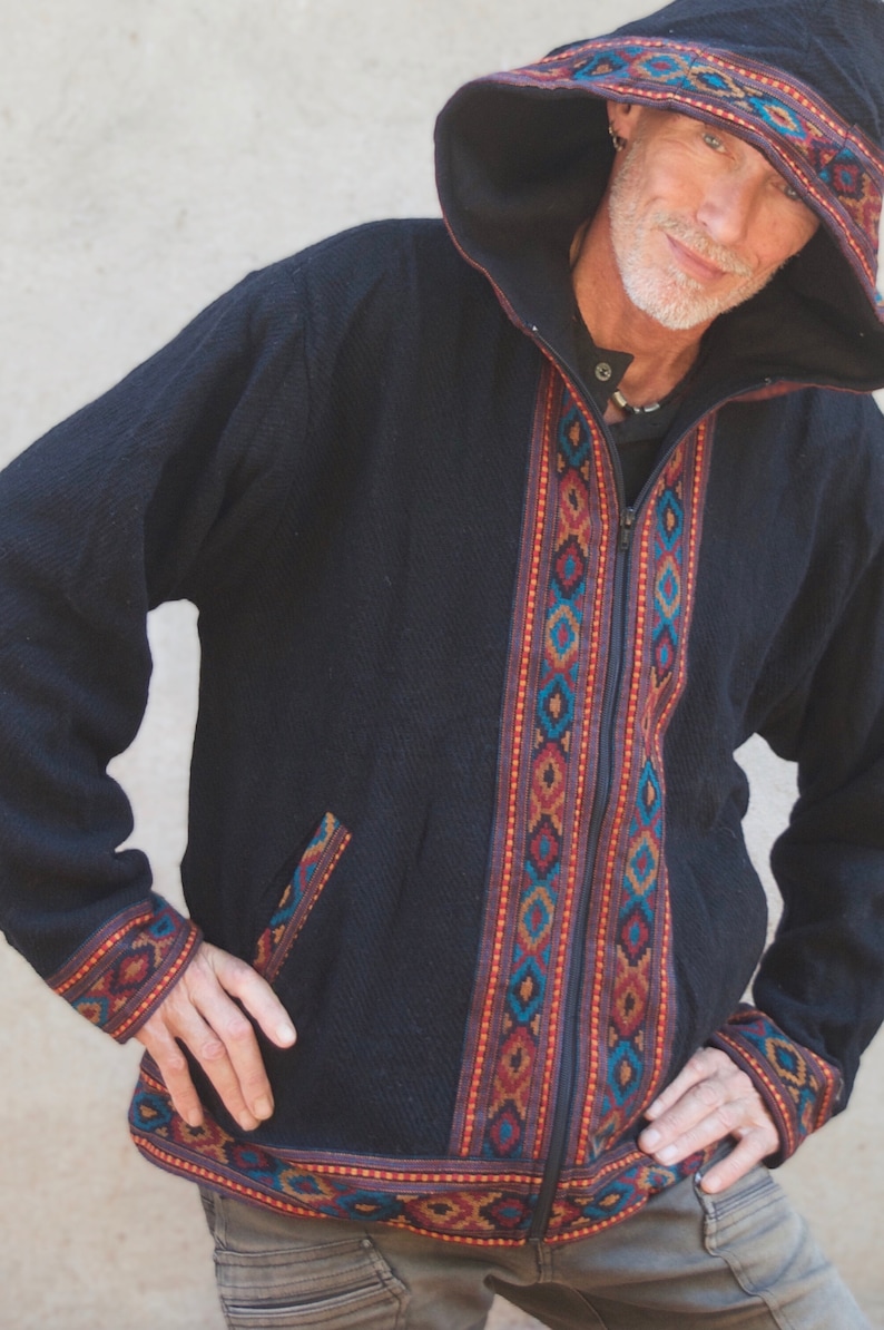 Puede incluir: Una chaqueta negra con capucha, cierre de cremallera y ribetes con estampado geom&eacute;trico de colores. La chaqueta tiene un bolsillo en el lado izquierdo.