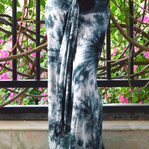 May include: Teal and white tie-dye trousers. The fabric is draped and knotted at the waist. The trousers are long and flowing, with a relaxed fit. The background includes a black metal railing and greenery.