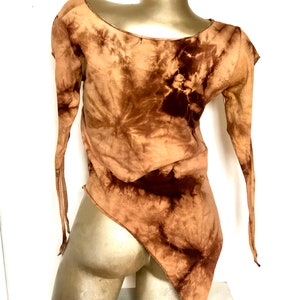 May include: A brown tie-dye top with long sleeves and an asymmetrical hemline. The top is displayed on a mannequin. The fabric has a swirling pattern of light and dark brown hues, creating a unique visual texture. The sleeves are long and end in thin ties.