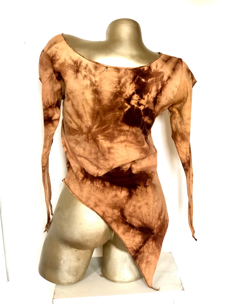 May include: A brown tie-dye top with long sleeves and an asymmetrical hemline. The top is displayed on a mannequin. The fabric has a swirling pattern of light and dark brown hues, creating a unique visual texture. The sleeves are long and end in thin ties.