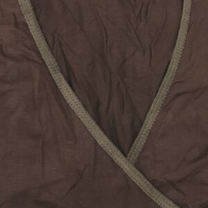 May include: A brown wrap top with a V-neck design. The top has a darker brown trim along the neckline and edges. The fabric appears soft and slightly textured.