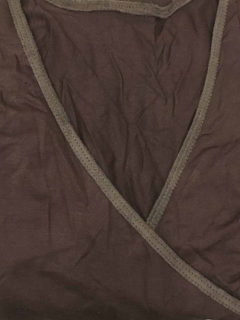 May include: A brown wrap top with a V-neck design. The top has a darker brown trim along the neckline and edges. The fabric appears soft and slightly textured.