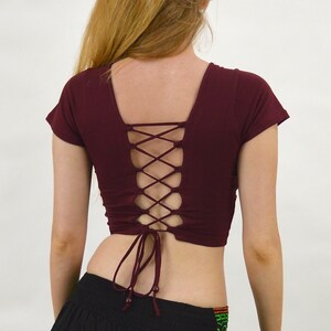 May include: A maroon crop top with short sleeves and a lace-up back. The top is tied at the waist.