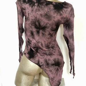 May include: A mauve and black tie-dye long-sleeve top with an asymmetrical hemline. The top has a one-shoulder design and is displayed on a mannequin. The fabric appears lightweight and flowing, with a dark, swirling pattern.