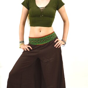 May include: A woman wearing a green crop top with a lace-up detail and brown wide-leg pants with a colorful embroidered waistband.