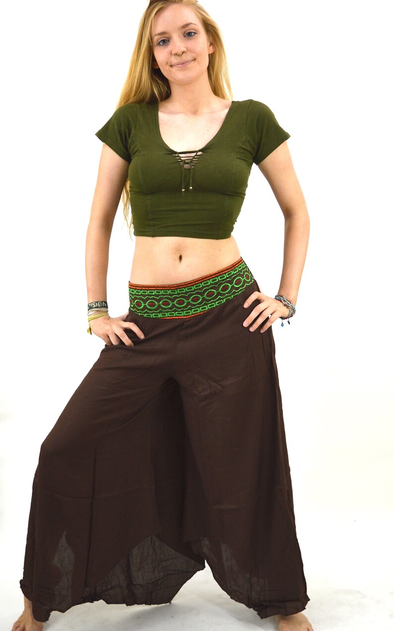 May include: A woman wearing a green crop top with a lace-up detail and brown wide-leg pants with a colorful embroidered waistband.