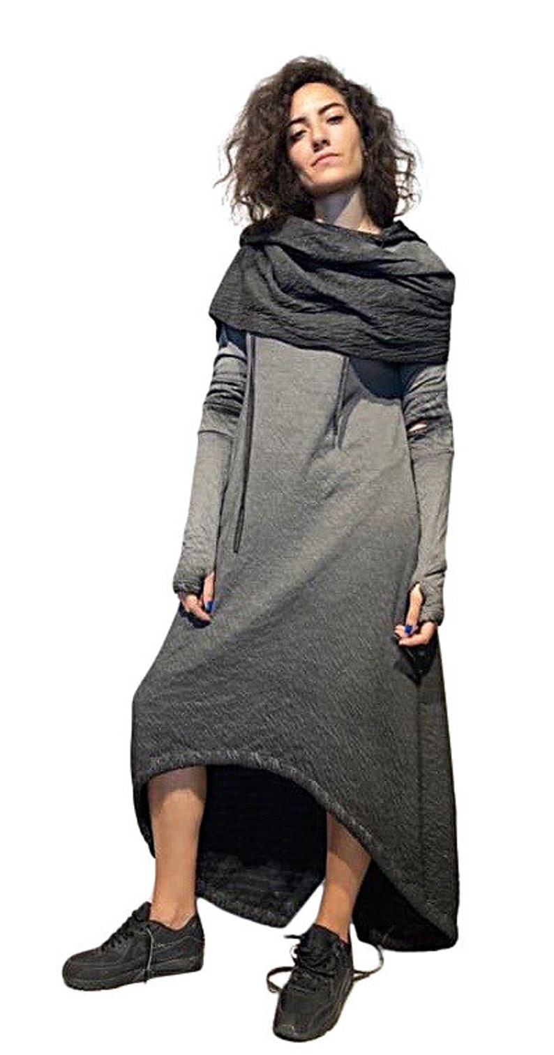Puede incluir: Un vestido largo gris con capucha y mangas largas. El vestido tiene un dobladillo alto-bajo y se combina con zapatillas negras. Una bufanda gris oscuro est&aacute; drapeada alrededor del cuello.