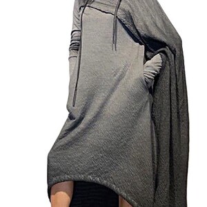 Puede incluir: Vestido gris con capucha y dise&ntilde;o tipo capa. El vestido presenta mangas largas, cuello alto y detalle de cord&oacute;n. La modelo lleva zapatillas negras. El vestido tiene un dobladillo asim&eacute;trico y fluido.