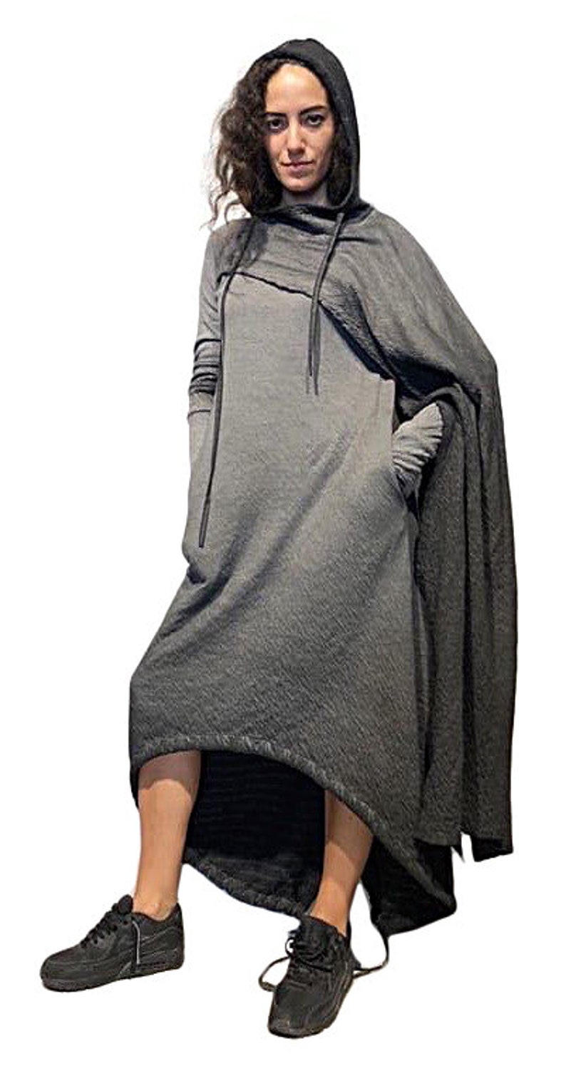 Puede incluir: Vestido gris con capucha y dise&ntilde;o tipo capa. El vestido presenta mangas largas, cuello alto y detalle de cord&oacute;n. La modelo lleva zapatillas negras. El vestido tiene un dobladillo asim&eacute;trico y fluido.