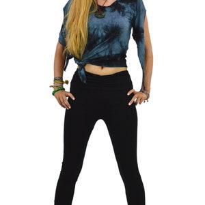 May include: A woman wearing a tie-dye top and black leggings. The top is a dark blue with a swirling pattern, tied at the waist. The leggings are form-fitting and black. The outfit is casual and comfortable.