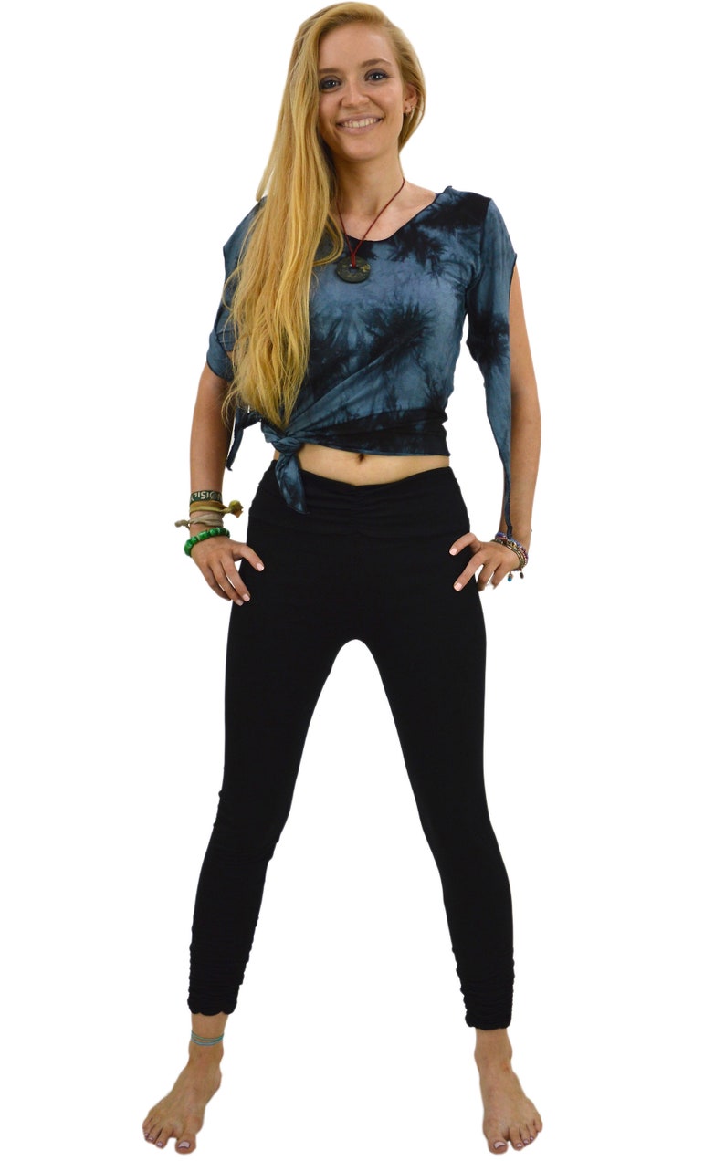 May include: A woman wearing a tie-dye top and black leggings. The top is a dark blue with a swirling pattern, tied at the waist. The leggings are form-fitting and black. The outfit is casual and comfortable.