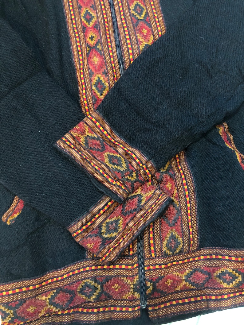 Puede incluir: Chaqueta negra con cierre de cremallera y ribetes de colores con patrones geom&eacute;tricos.