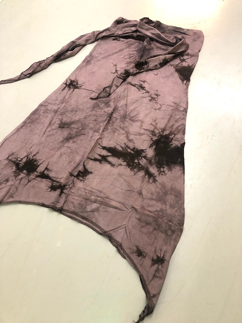 May include: A mauve and black tie-dye skirt. The skirt features an asymmetrical cut and a long tie. The fabric is lightweight and has a crinkled texture. The skirt's length is approximately 100 cm.