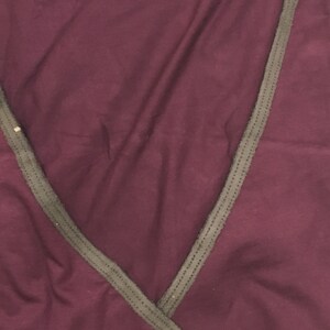 May include: A burgundy wrap top with a contrasting dark gray trim along the neckline and edges. The fabric appears soft and drapes gently. The top has a V-neck design.