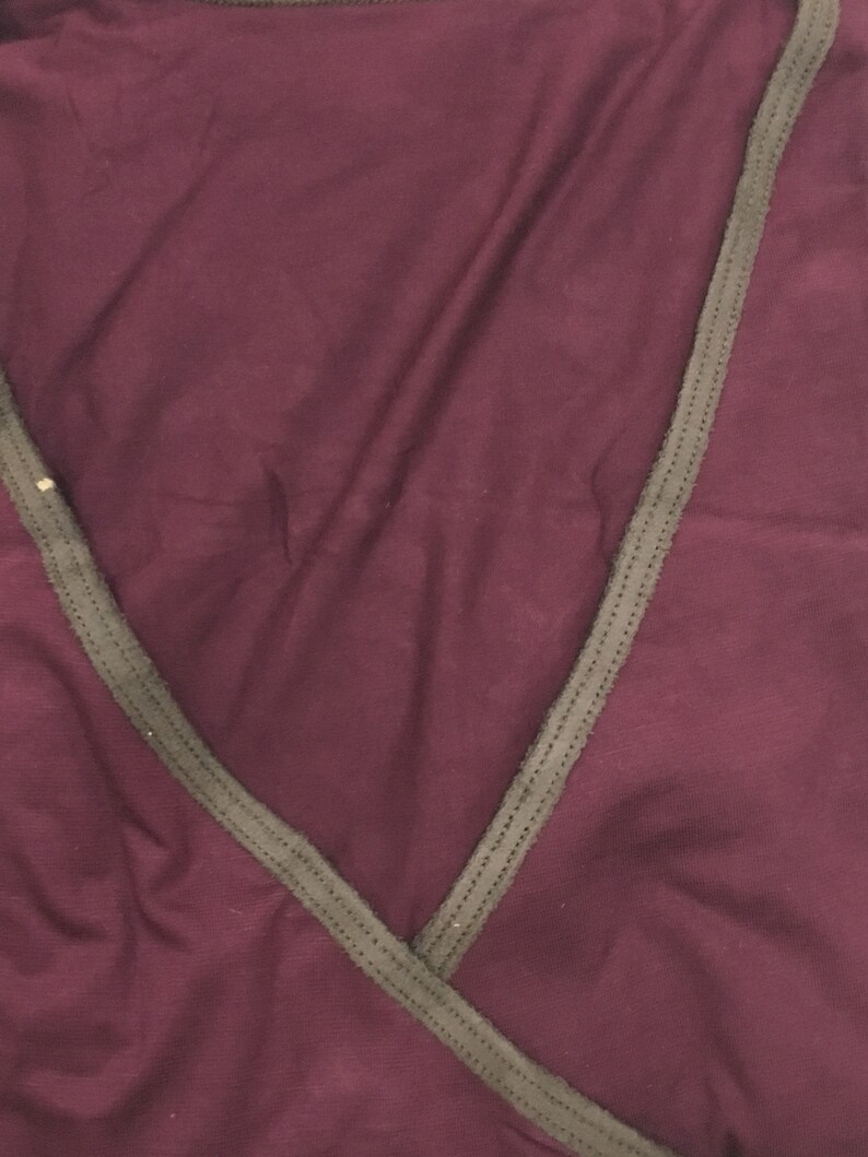 May include: A burgundy wrap top with a contrasting dark gray trim along the neckline and edges. The fabric appears soft and drapes gently. The top has a V-neck design.