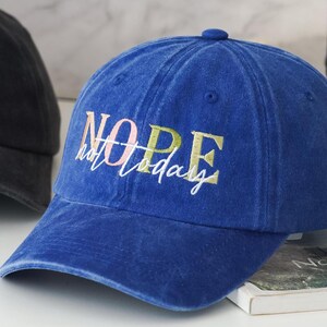 May include: A blue denim baseball cap with the text "NOPE not today" embroidered in white, pink, and green.