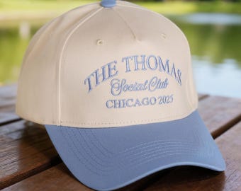 Puede incluir: Gorra de béisbol con corona color crema y visera azul claro. El texto "THE THOMAS Social Club CHICAGO 2025" está bordado en azul claro en la parte delantera. La gorra tiene un botón en la parte superior.